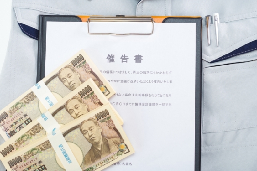 ポケットにペンがさしてある作業着の上に100万円札束3束とバインダーに挟まれた催告書